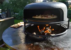 De nieuwe Pizzaoven van Ofyr, dat bestaat uit een tweezijdige gietijzeren plaat, een pizzasteen daarboven geplaatst en een dubbelwandige stalen cloche. De buitenrand roteert rond de binnenzijde.